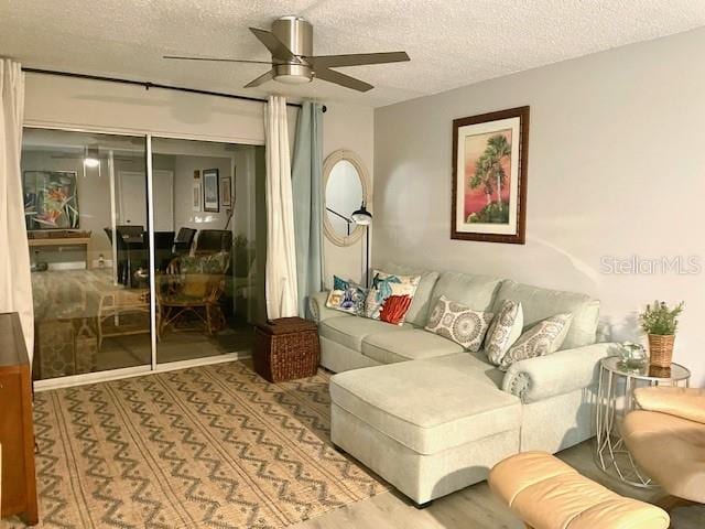 living room with a textured ceiling, light wood-type flooring, and ceiling fan