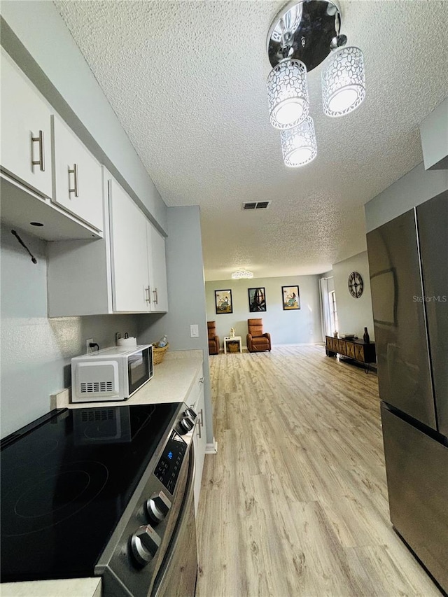 kitchen featuring white cabinetry, stainless steel appliances, light wood-type flooring, and a textured ceiling