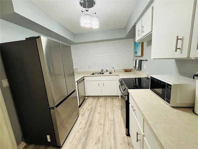 kitchen featuring appliances with stainless steel finishes, white cabinetry, a textured ceiling, light wood-type flooring, and sink