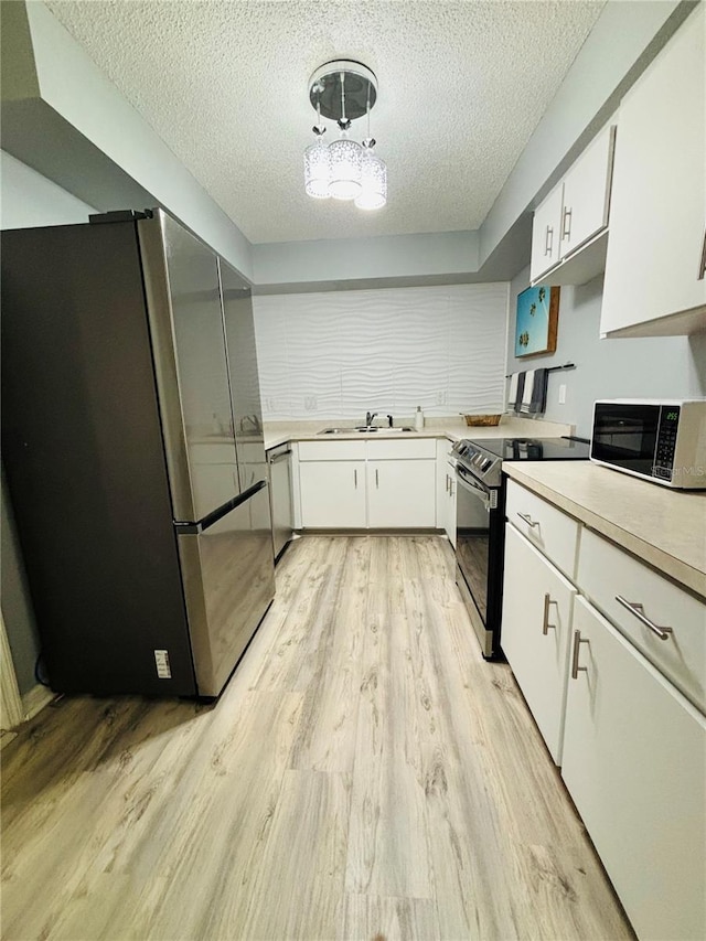 kitchen with white cabinets, a textured ceiling, pendant lighting, light hardwood / wood-style floors, and stainless steel appliances