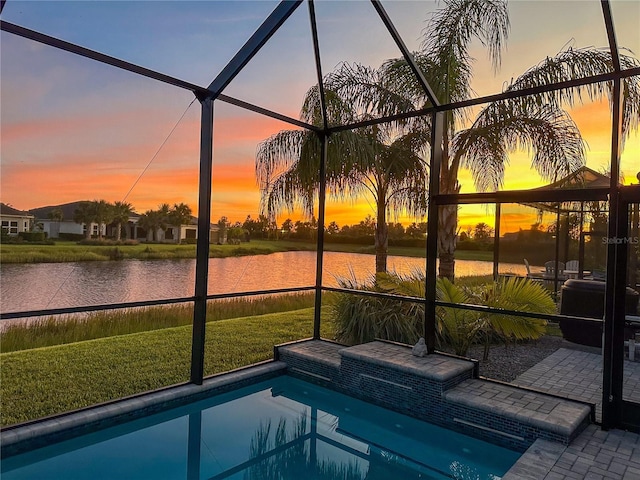 pool at dusk with a water view, a patio area, a lanai, and a lawn