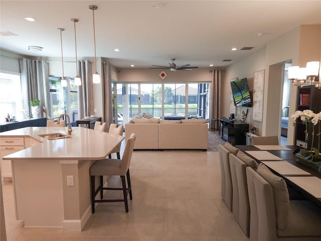 kitchen with a center island with sink, hanging light fixtures, ceiling fan, a kitchen breakfast bar, and sink