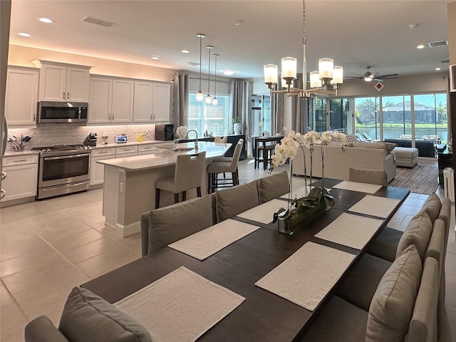 dining area featuring sink, ceiling fan with notable chandelier, a healthy amount of sunlight, and light tile patterned floors