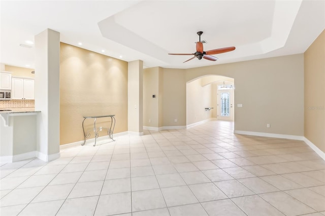 tiled empty room with ceiling fan and a raised ceiling