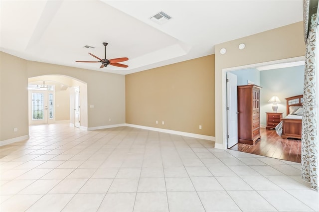 empty room featuring ceiling fan, light tile patterned floors, a raised ceiling, and french doors