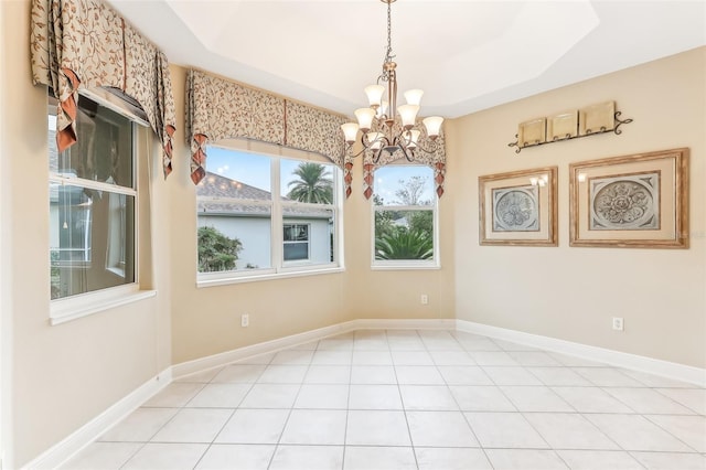 empty room with an inviting chandelier, baseboards, a raised ceiling, and light tile patterned flooring