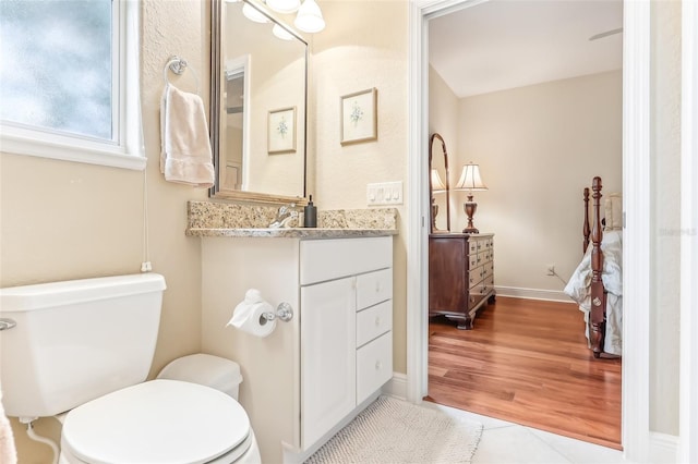 bathroom with baseboards, connected bathroom, toilet, wood finished floors, and vanity