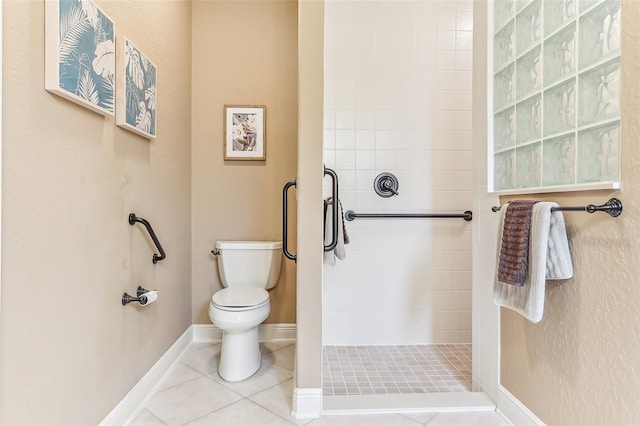 bathroom featuring tile patterned flooring, a tile shower, toilet, and baseboards