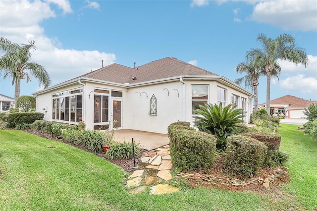 rear view of house featuring a garage, a sunroom, a yard, stucco siding, and a patio area