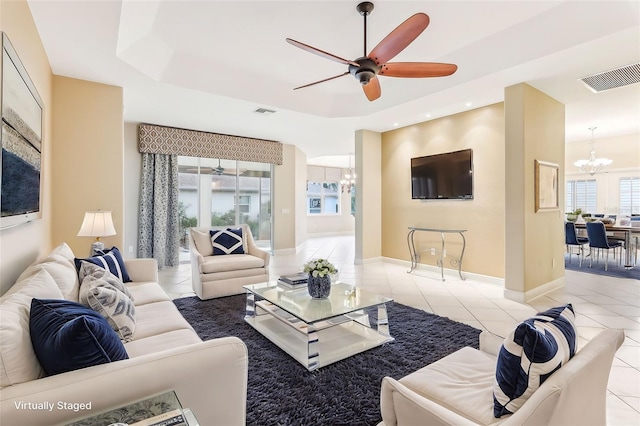 living room featuring light tile patterned floors, a tray ceiling, ceiling fan with notable chandelier, and visible vents