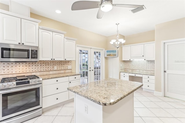 kitchen featuring light stone counters, light tile patterned flooring, stainless steel appliances, white cabinetry, and decorative light fixtures