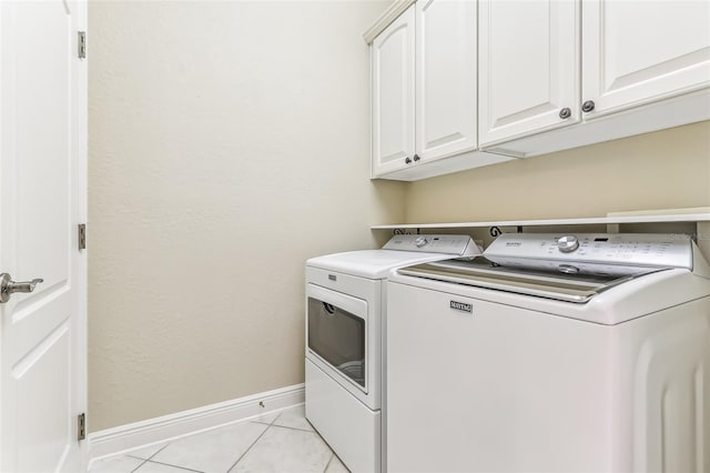 clothes washing area featuring light tile patterned floors, washing machine and dryer, and cabinets