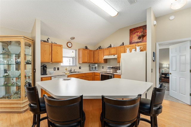 kitchen featuring white appliances, light wood-type flooring, a textured ceiling, a kitchen breakfast bar, and vaulted ceiling