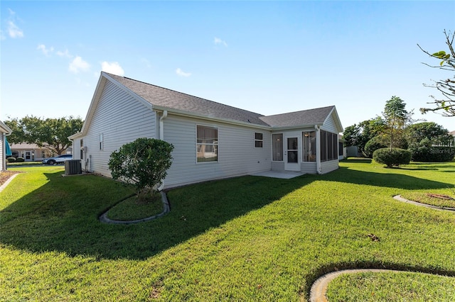 rear view of house featuring central air condition unit, a sunroom, and a lawn