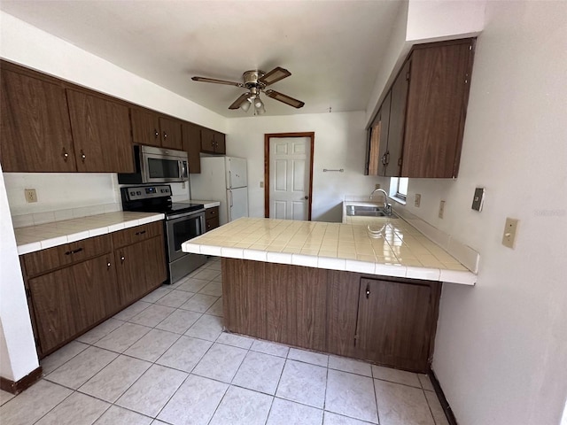 kitchen featuring kitchen peninsula, dark brown cabinets, tile countertops, sink, and stainless steel appliances