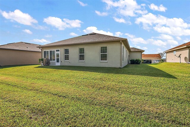 back of house with stucco siding and a yard