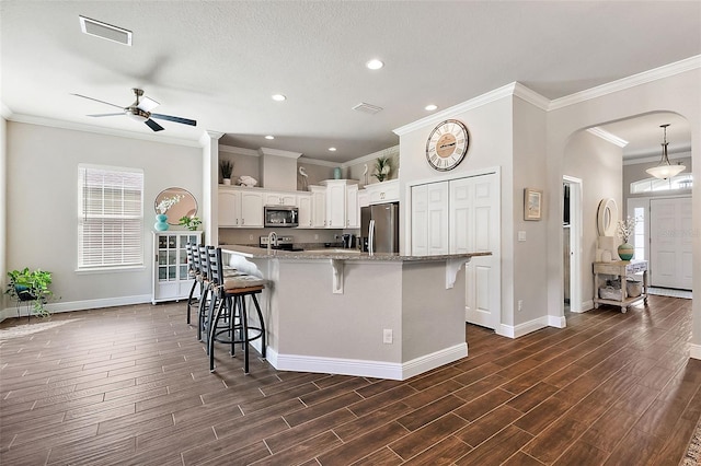 kitchen featuring a kitchen breakfast bar, stainless steel appliances, light stone countertops, white cabinetry, and dark hardwood / wood-style flooring