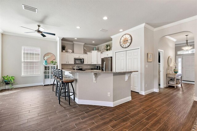 kitchen featuring arched walkways, stainless steel appliances, a ceiling fan, a kitchen bar, and visible vents
