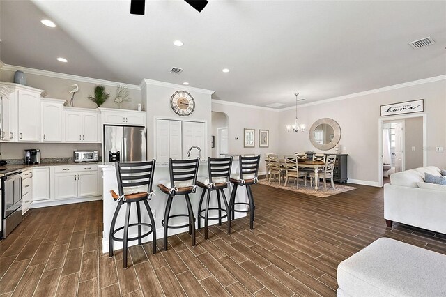 kitchen featuring ornamental molding, appliances with stainless steel finishes, ceiling fan with notable chandelier, and a breakfast bar