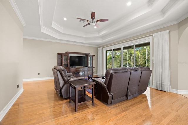 living area with baseboards, light wood-style flooring, ceiling fan, crown molding, and a raised ceiling