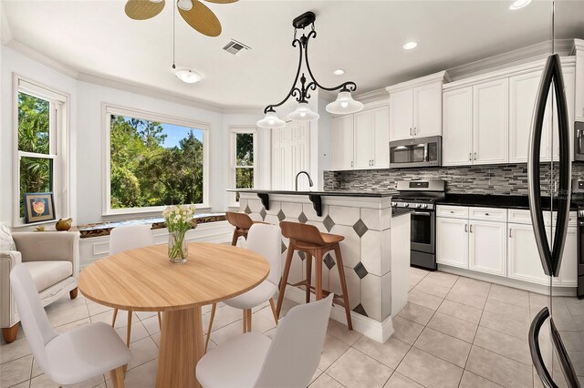 kitchen with light tile patterned flooring, a center island with sink, appliances with stainless steel finishes, pendant lighting, and white cabinets