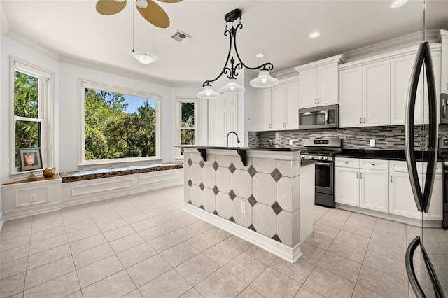 kitchen featuring a kitchen island with sink, decorative light fixtures, stainless steel appliances, and white cabinets