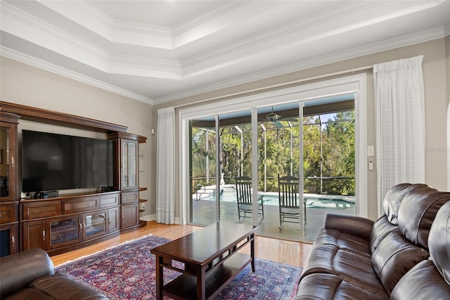 living area featuring a tray ceiling, light wood-style flooring, and ornamental molding