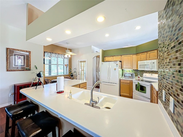 kitchen featuring sink, a breakfast bar, backsplash, white appliances, and pendant lighting