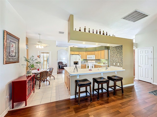 kitchen with tasteful backsplash, white appliances, kitchen peninsula, ceiling fan, and light hardwood / wood-style flooring