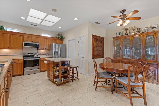 kitchen with decorative backsplash, a skylight, stainless steel appliances, ceiling fan, and a center island