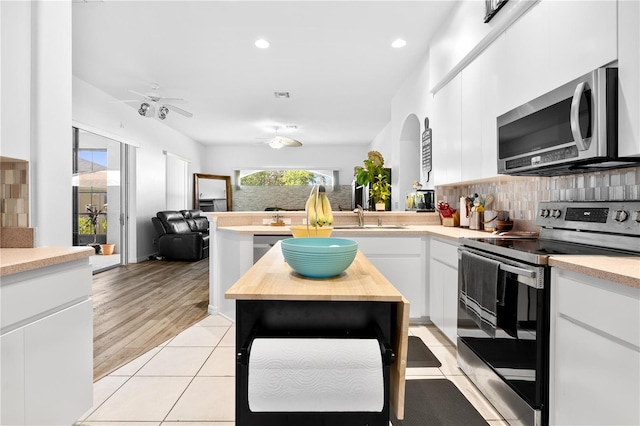 kitchen with white cabinets, tasteful backsplash, ceiling fan, appliances with stainless steel finishes, and light hardwood / wood-style floors