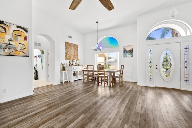 foyer entrance with wood-type flooring, a high ceiling, and ceiling fan with notable chandelier