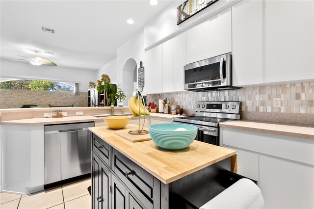 kitchen with light tile patterned floors, appliances with stainless steel finishes, backsplash, white cabinetry, and a center island