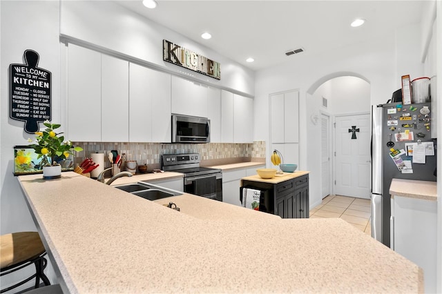 kitchen featuring appliances with stainless steel finishes, kitchen peninsula, a breakfast bar area, white cabinetry, and light tile patterned floors