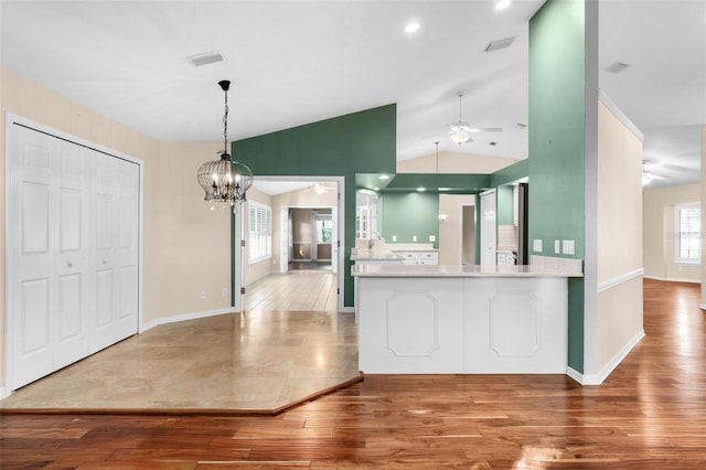 kitchen with kitchen peninsula, hardwood / wood-style floors, vaulted ceiling, pendant lighting, and a notable chandelier