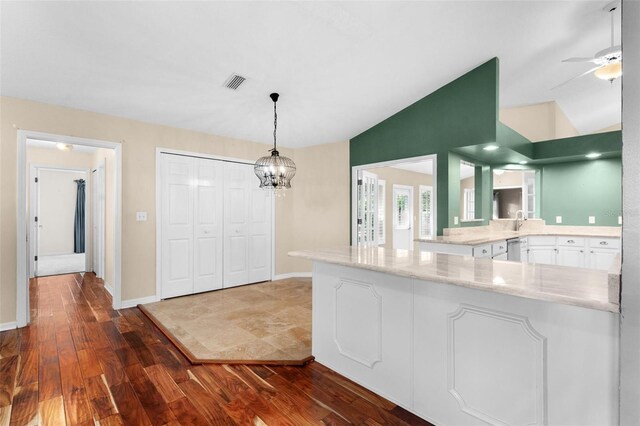 kitchen featuring kitchen peninsula, white cabinetry, vaulted ceiling, dark wood-type flooring, and decorative light fixtures