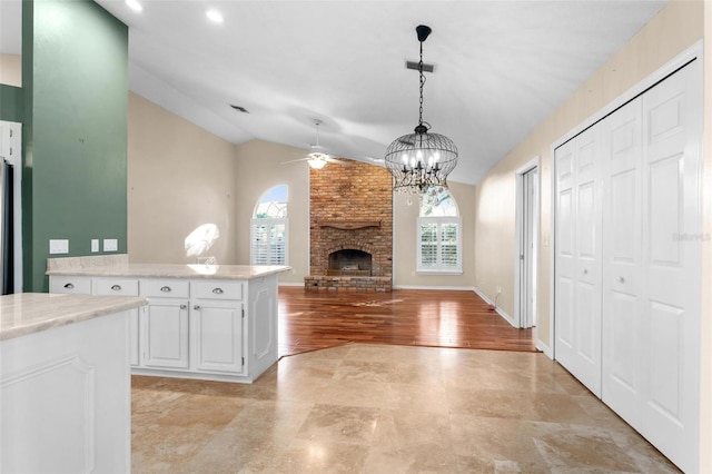 kitchen with vaulted ceiling, a brick fireplace, pendant lighting, light wood-type flooring, and white cabinetry