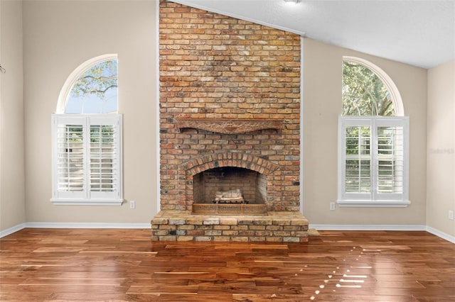 unfurnished living room with lofted ceiling, a brick fireplace, and wood-type flooring