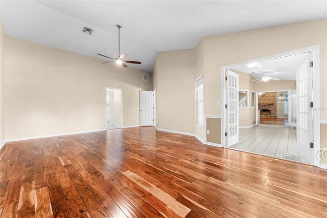 unfurnished living room featuring ceiling fan, a stone fireplace, vaulted ceiling, and light wood-type flooring