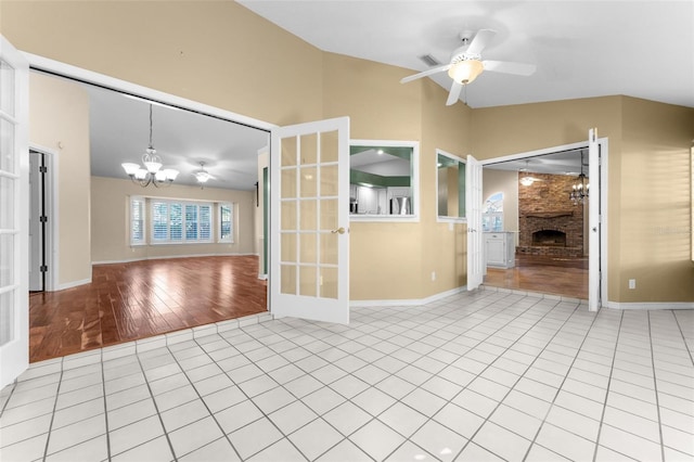 spare room featuring ceiling fan with notable chandelier, a fireplace, french doors, vaulted ceiling, and hardwood / wood-style flooring