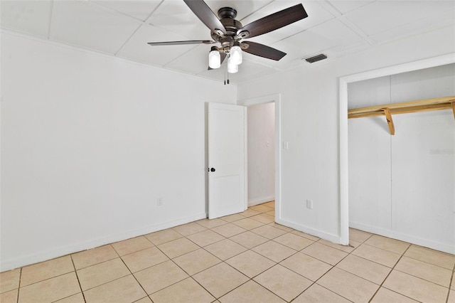 unfurnished bedroom with a drop ceiling, light tile patterned flooring, a closet, and ceiling fan