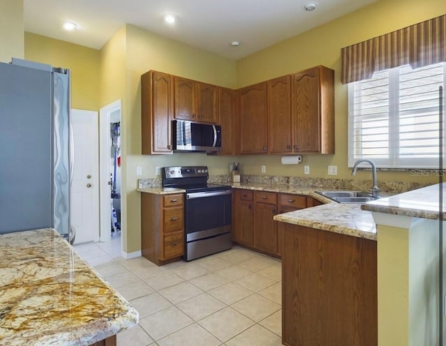 kitchen featuring light tile patterned flooring, sink, kitchen peninsula, stainless steel appliances, and light stone countertops