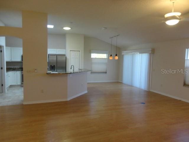 unfurnished living room featuring sink, light hardwood / wood-style floors, vaulted ceiling, and an inviting chandelier