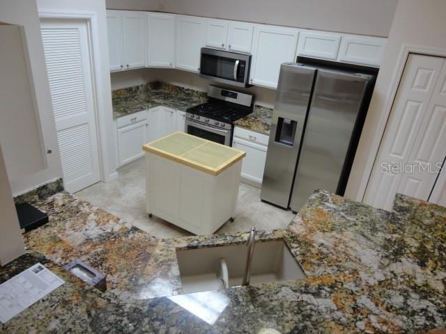 kitchen with appliances with stainless steel finishes, kitchen peninsula, white cabinetry, and dark stone counters