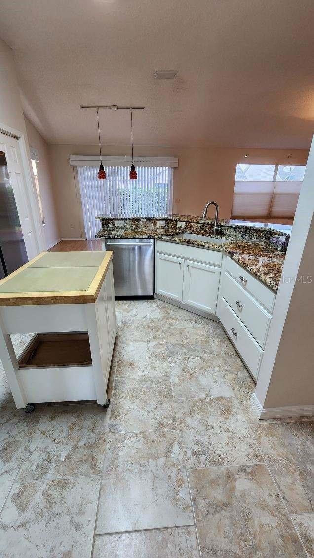 kitchen with white cabinets, hanging light fixtures, stainless steel dishwasher, dark stone counters, and sink