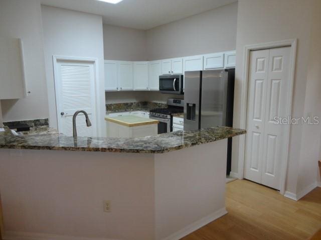 kitchen featuring kitchen peninsula, white cabinets, dark stone counters, light hardwood / wood-style floors, and stainless steel appliances