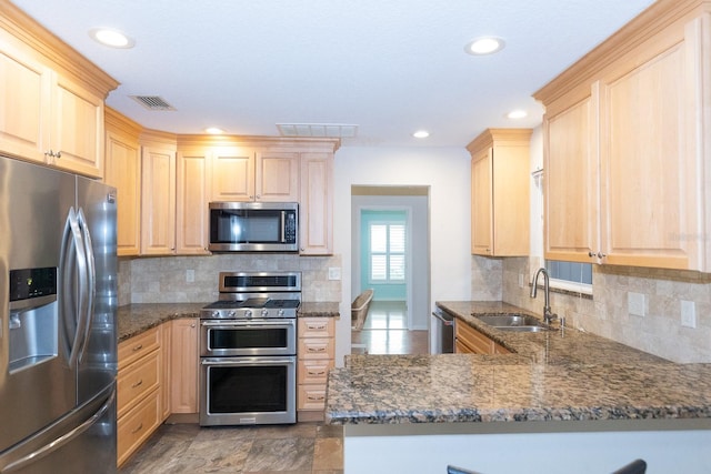 kitchen featuring kitchen peninsula, stainless steel appliances, sink, and dark stone countertops