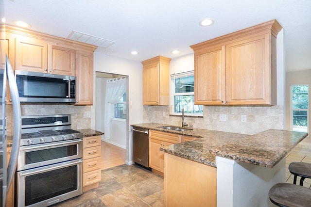 kitchen featuring kitchen peninsula, sink, tasteful backsplash, a breakfast bar, and appliances with stainless steel finishes