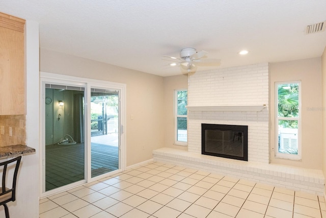 unfurnished living room with a fireplace, ceiling fan, and light tile patterned floors