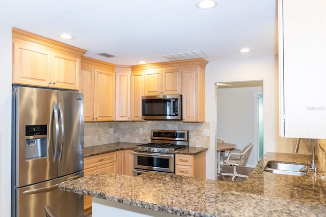 kitchen featuring stainless steel appliances, light brown cabinets, kitchen peninsula, and light stone counters